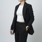 Person wearing a black blazer and black pants with a white top on a plain background