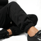 Person wearing black sweatpants and black Puma sneakers on a white background
