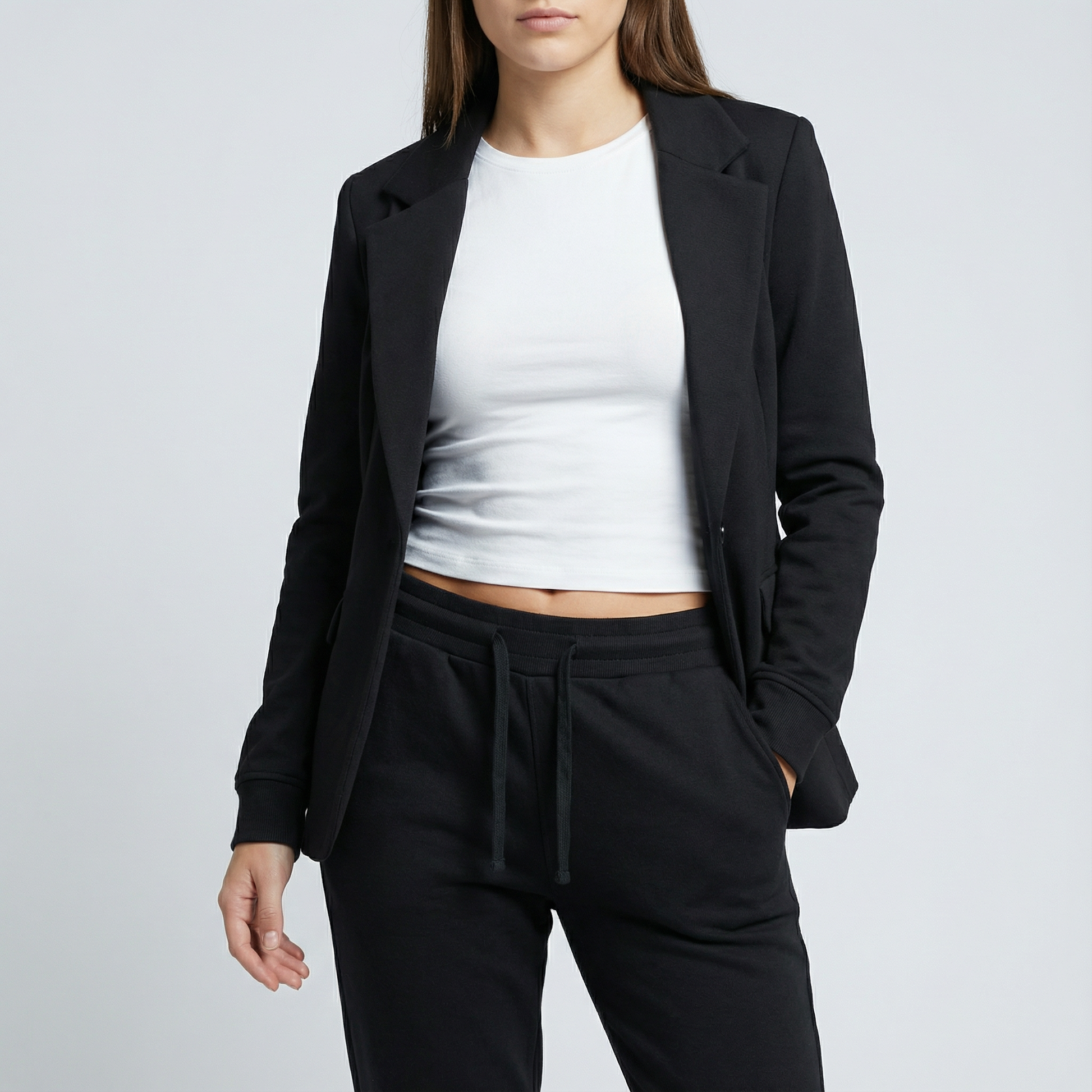 Person wearing a black blazer, white crop top, and black pants on a light gray background