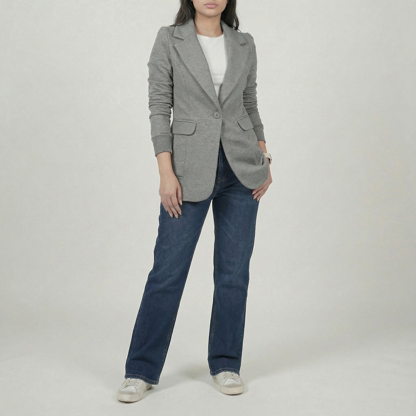 Person wearing a gray blazer and blue jeans on a plain background