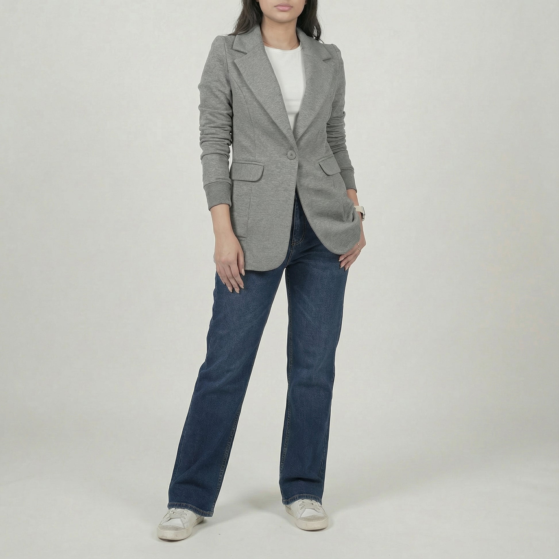 Person wearing a gray blazer and blue jeans on a plain background